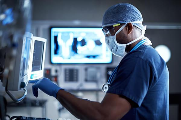 Surgeon uses a variety of digital electronics to monitor a patient in an operating room.